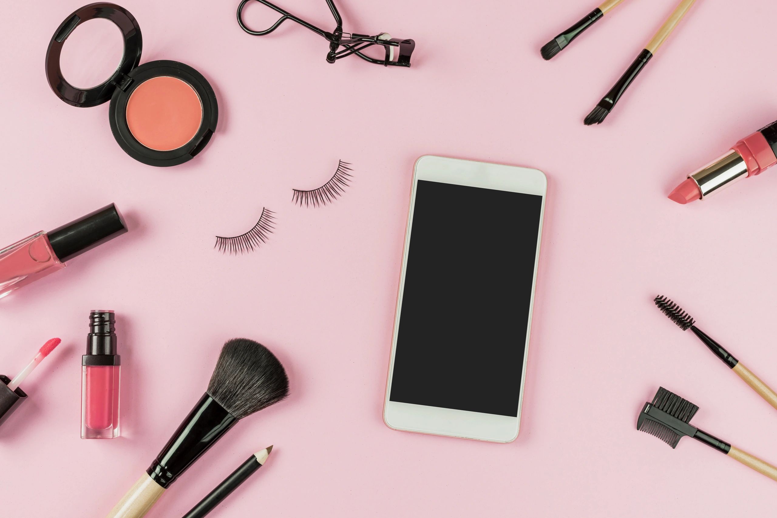Makeup brushes and cosmetics arranged neatly on a pink background